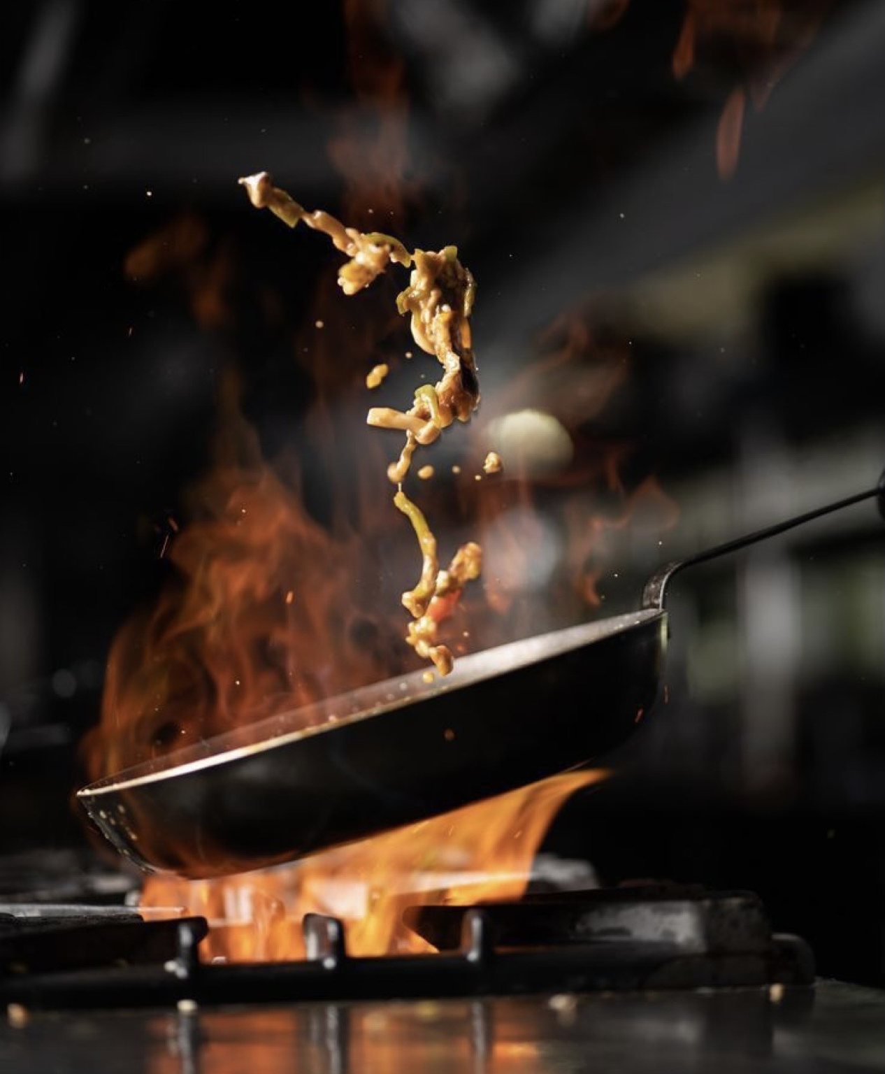 Frigideira sobre a chama com o yakisoba saltando no ar